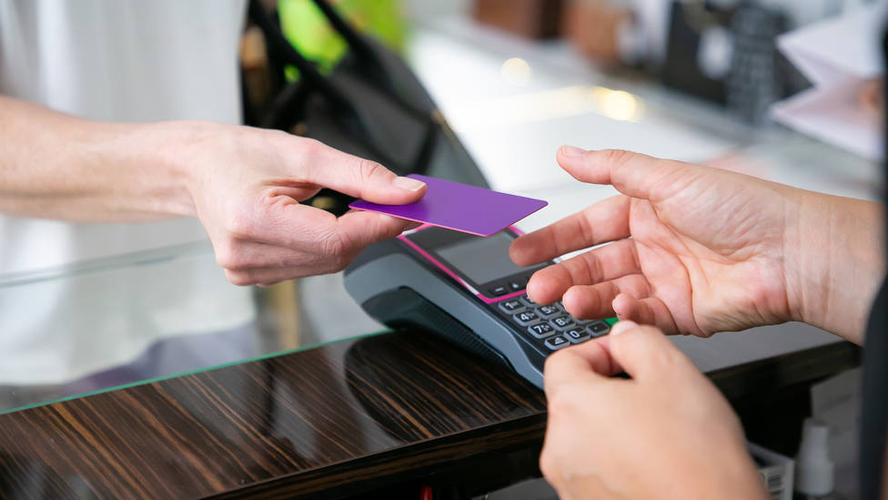 customer-giving-credit-card-to-cashier-over-desk-with-pos-terminal-for-payment-cropped-shot-closeup-of-hands